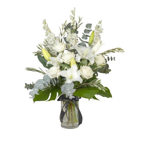 Vibrant white roses, delphiniums, and white oriental lilies, displayed amongst lush green monstera...