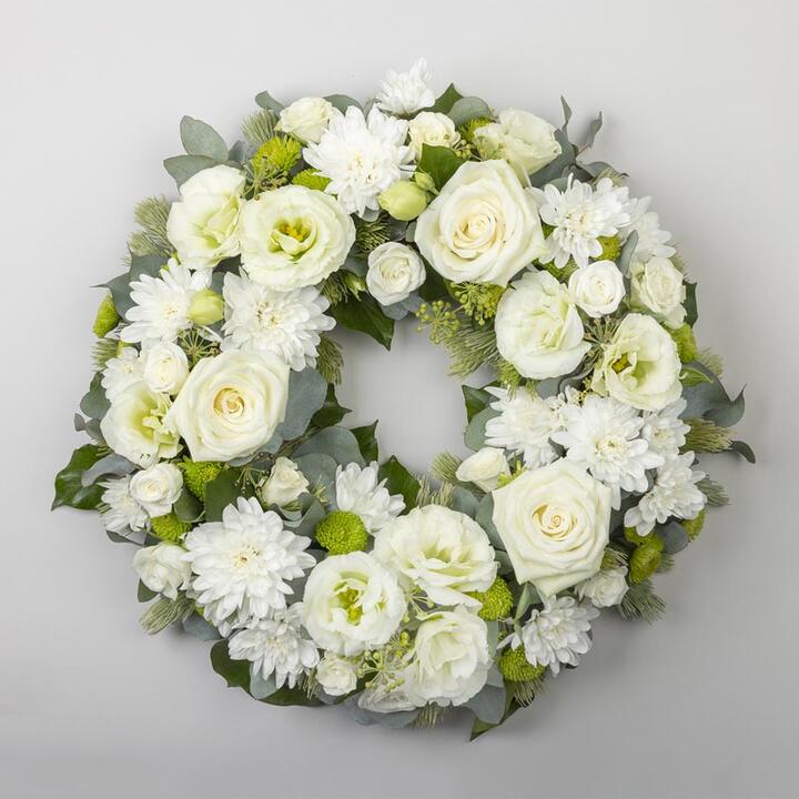 The White Sympathy Wreath is a peaceful arrangement of white roses, chrysanthemums, and verdant...