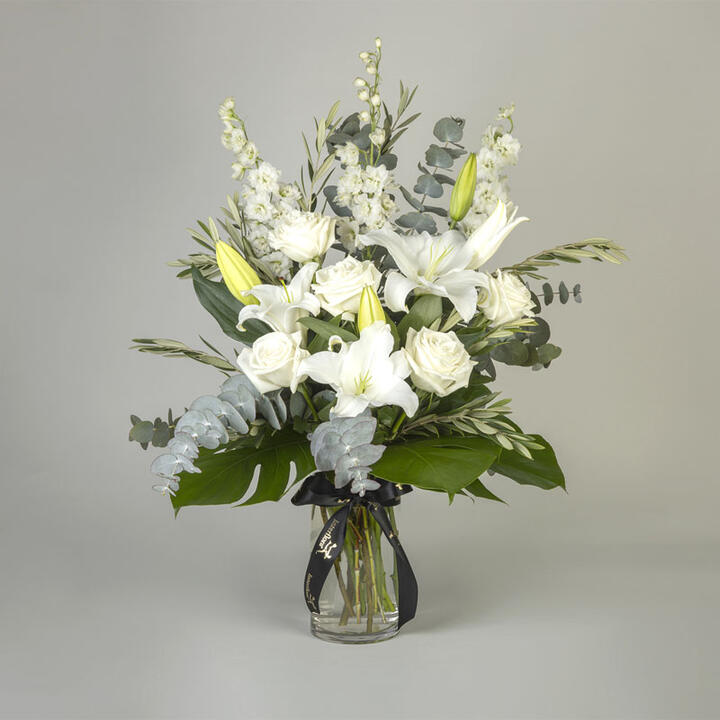 Vibrant white roses, delphiniums, and white oriental lilies, displayed amongst lush green monstera...