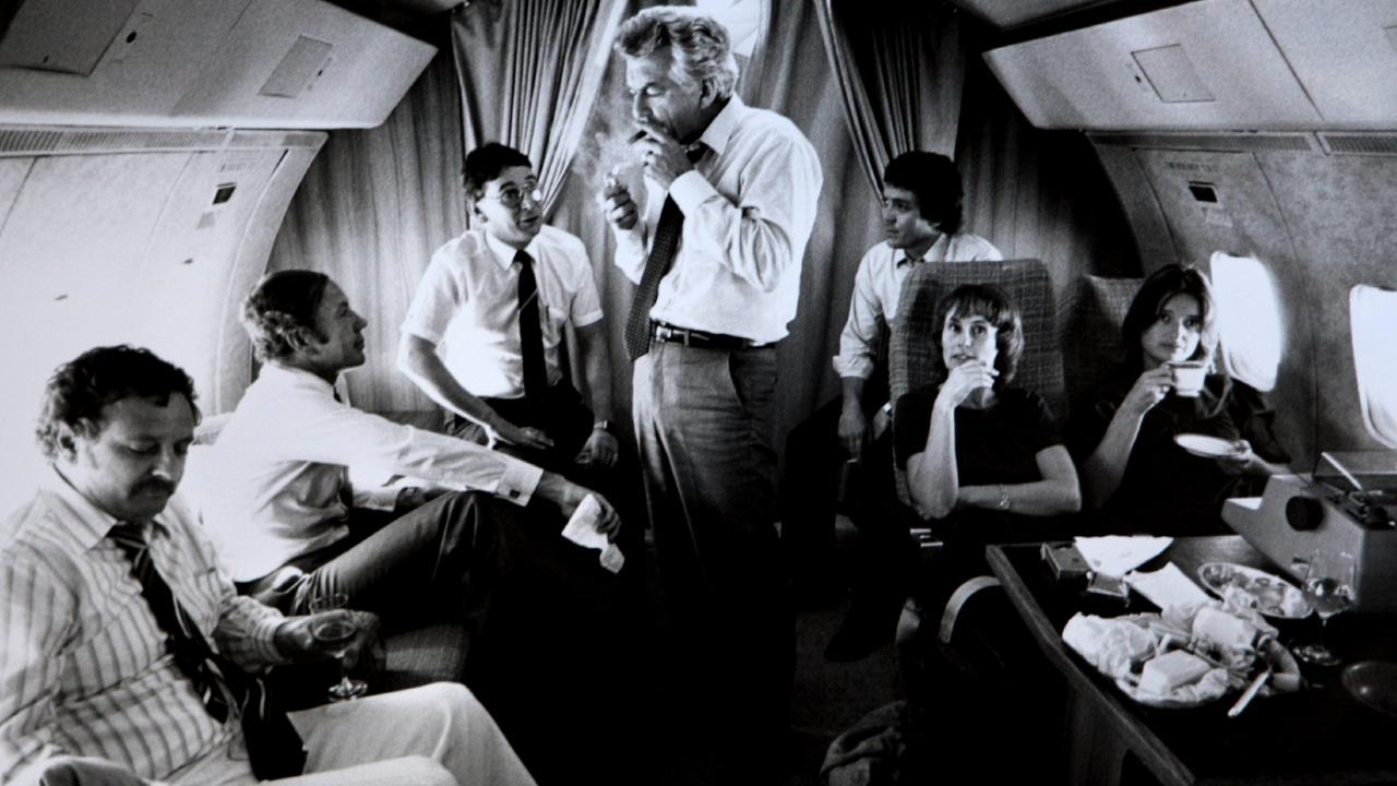 As opposition leader, Bob Hawke, with advisers and media, from left, journalist Colin Parks, Senator Kerry Sibraa, journalist Peter Logue, senior advisor Geoff Walsh and  staffers Kate Moore and Janet Willis, lights up a cigar on a VIP flight during the 1983 federal election campaign, when Labor was swept to a landslide victory.