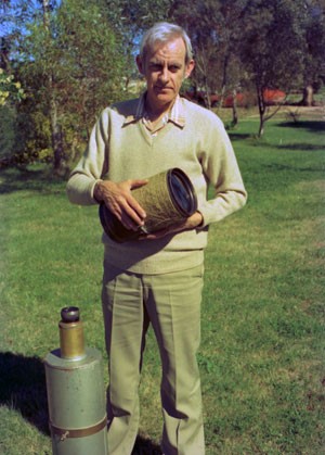 Bradfield holds the antique 6-inch lens that served as the objective of his comet seeker.  At lower left is the telescope's eye end, showing its large Erfle ocular of 1¼-inch focal length.  He used this telescope to discover all his early comets. Courtesy S&T: Dennis di Cicco

