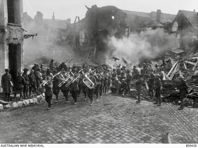 Image shows the Band of the 5th Australian Infantry Brigade, led by Bandmaster Sergeant A Peagam of the 19th Battalion, passing through the Grande Place (Town Square) of Bapaume, playing the 'Victoria March'.